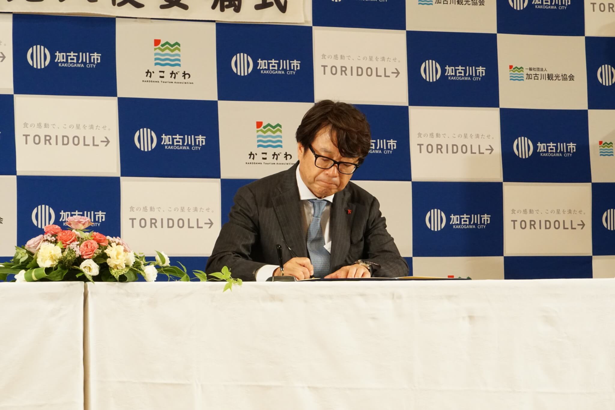 加古川市との包括連携協定の締結式でサインをする粟田貴也氏