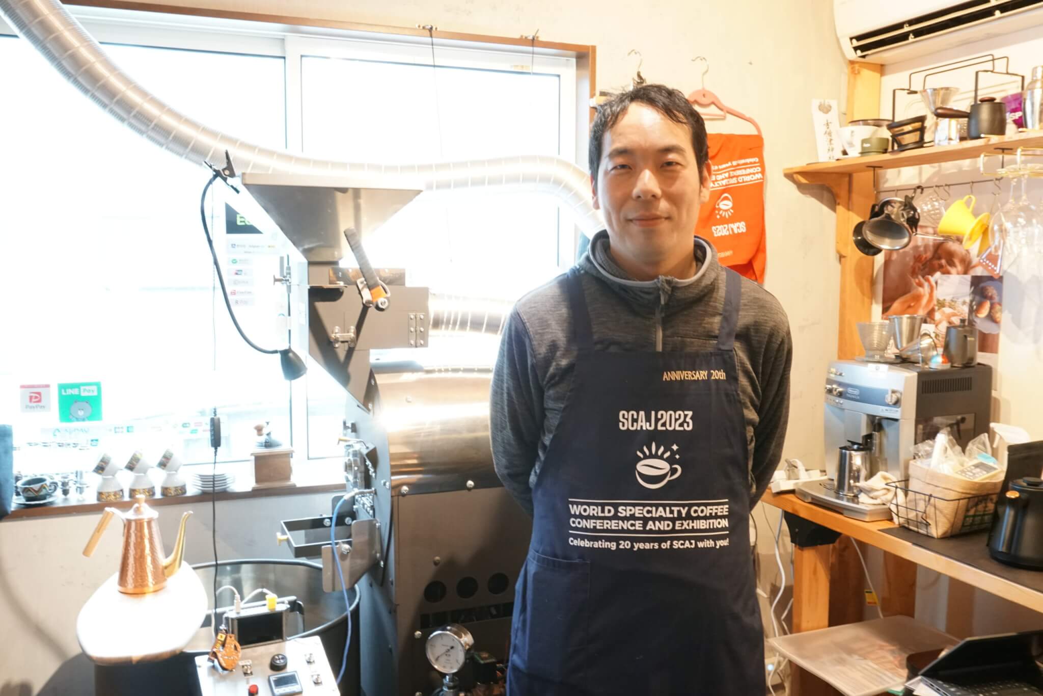 Kotobuki焙煎の店主の田村寿之さん。後ろには6kgの焙煎機。2024年3月12日撮影