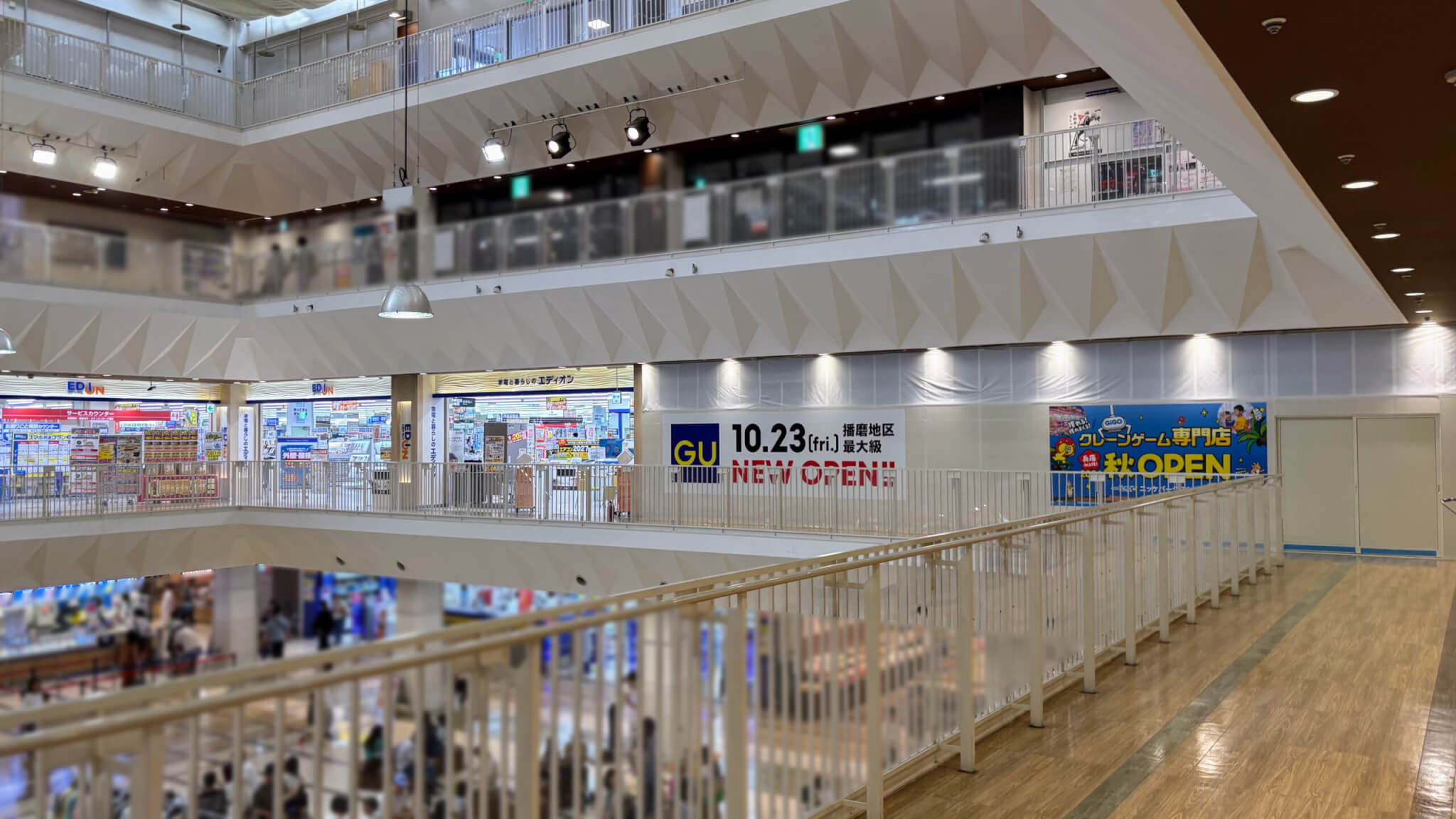 ニッケパークタウンの吹き抜けから見た2階のエディオンと、その並びに掲示されたGUの10月23日オープン告知